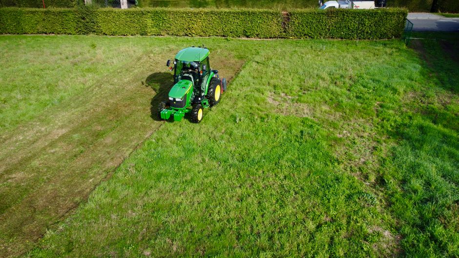 Worker mowing lawn and trimming shrubs in a yard