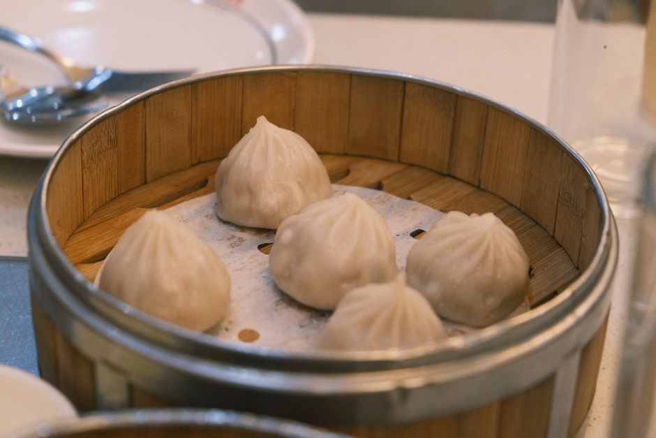 Restaurant interior with chefs preparing dumplings and bao in an open kitchen.