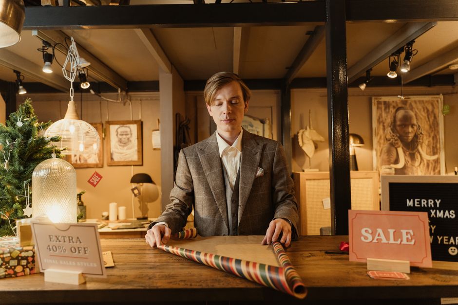 A smiling shopkeeper arranging gifts and greeting cards on a shelf