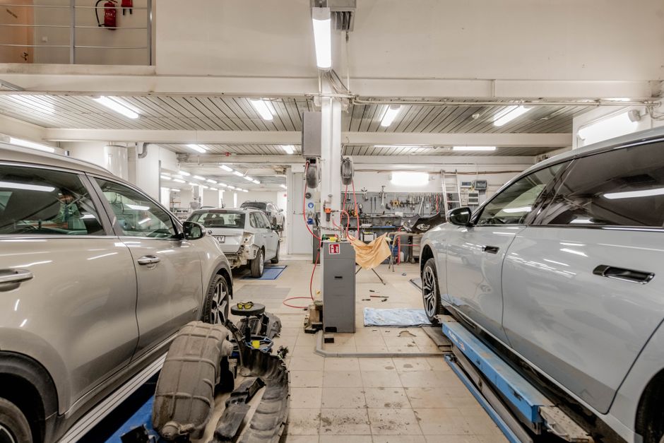 Technicians performing frame repair on a vehicle inside an auto body workshop